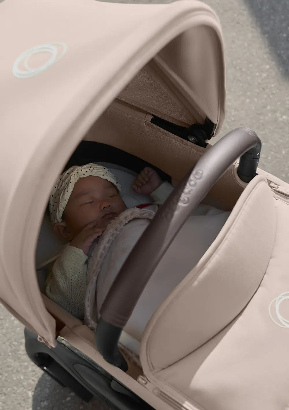 Ein schlafendes Neugeborenes liegt geborgen in der beigefarbenen Bugaboo Liegewanne für den Kinderwagen Dragonfly Plus.