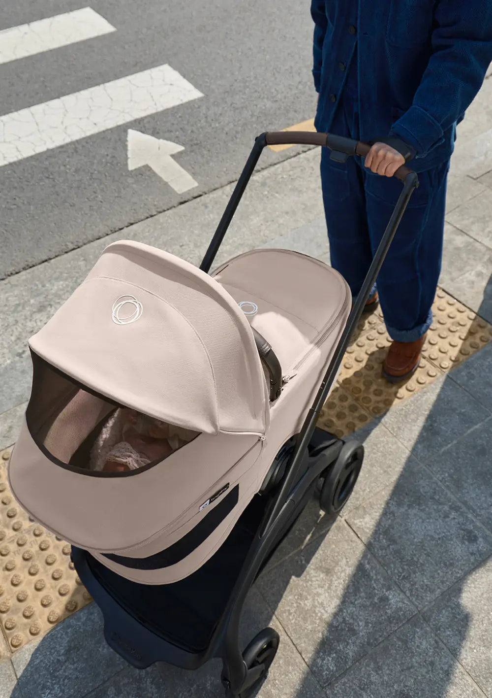 Draufsicht auf den Kinderwagen in Fahrtrichtung: Das geöffnete Mesh-Lüftungsfenster am Verdeck der Bugaboo Liegewanne für den Kinderwagen Dragonfly Plus gibt den Blick auf das Baby frei.