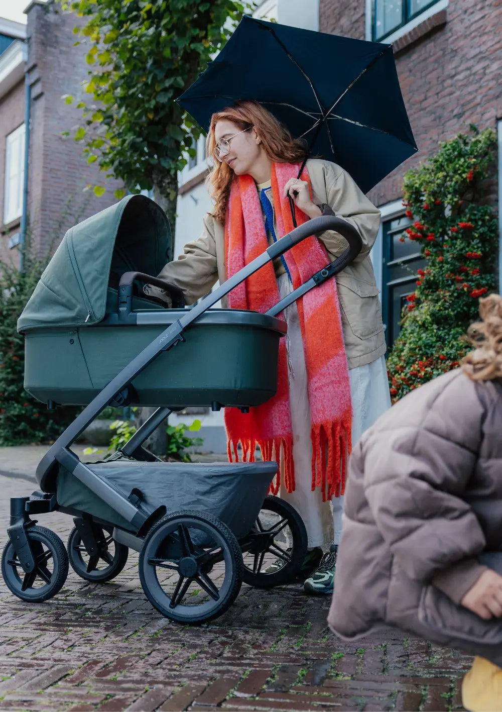 Frau mit Regenschirm streichelt Baby in Babywanne des Joolz Kinderwagen-Sets 'Geo5' Single Forest Green