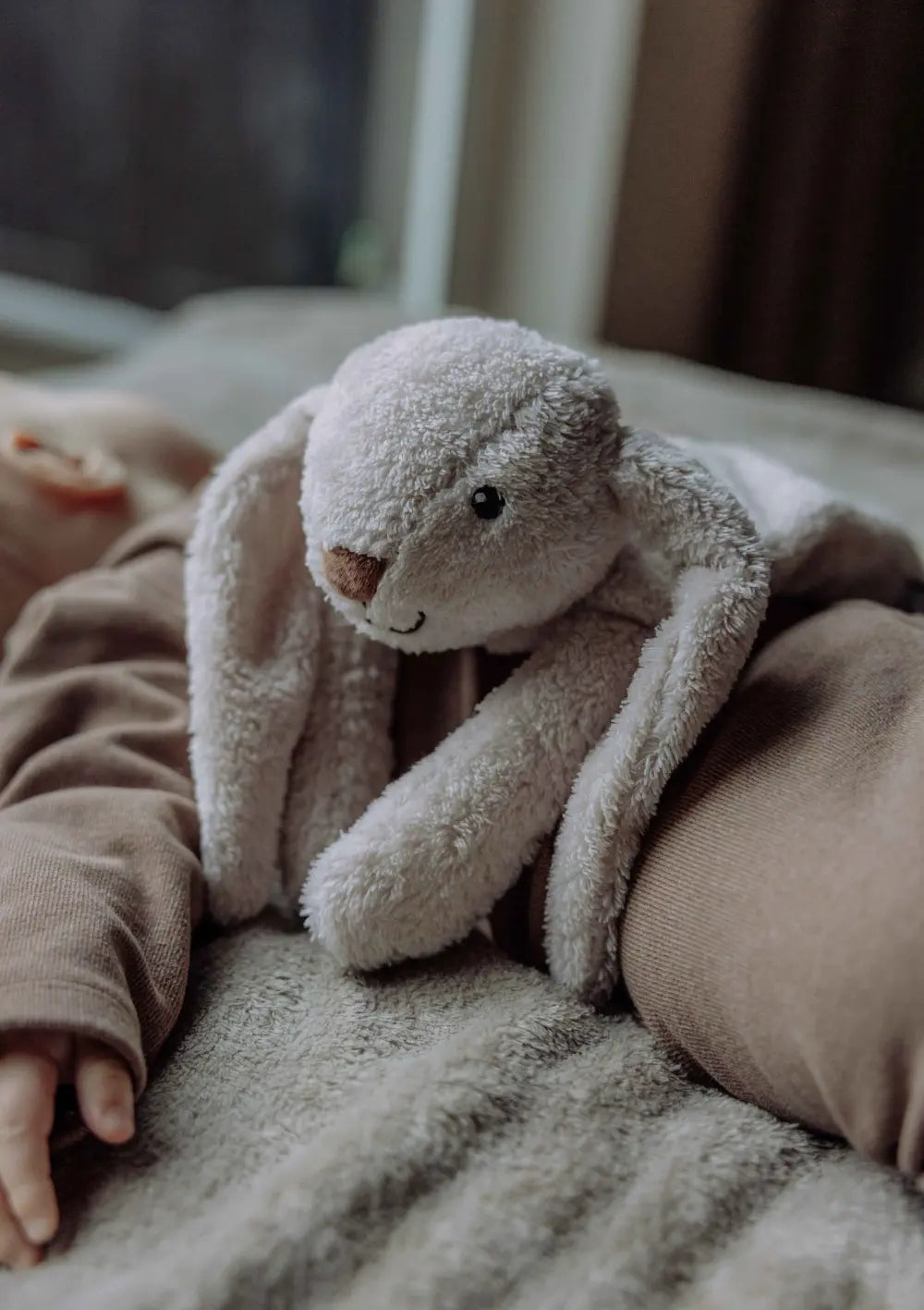 Baby liegt im Bett mit dem flow AMSTERDAM Wärmekissen Hase 'Milo' blush auf dem Bauch