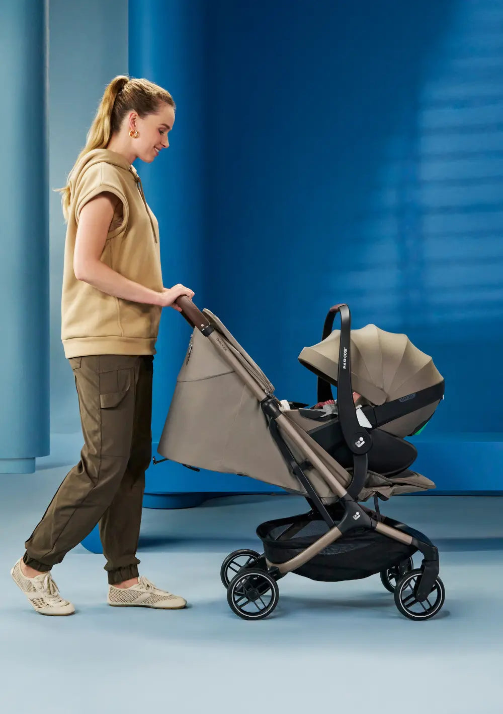 Frau schiebt Baby in Babyschale, befestigt am Maxi-Cosi Buggy 'Oxford Cabin' Oak Truffle