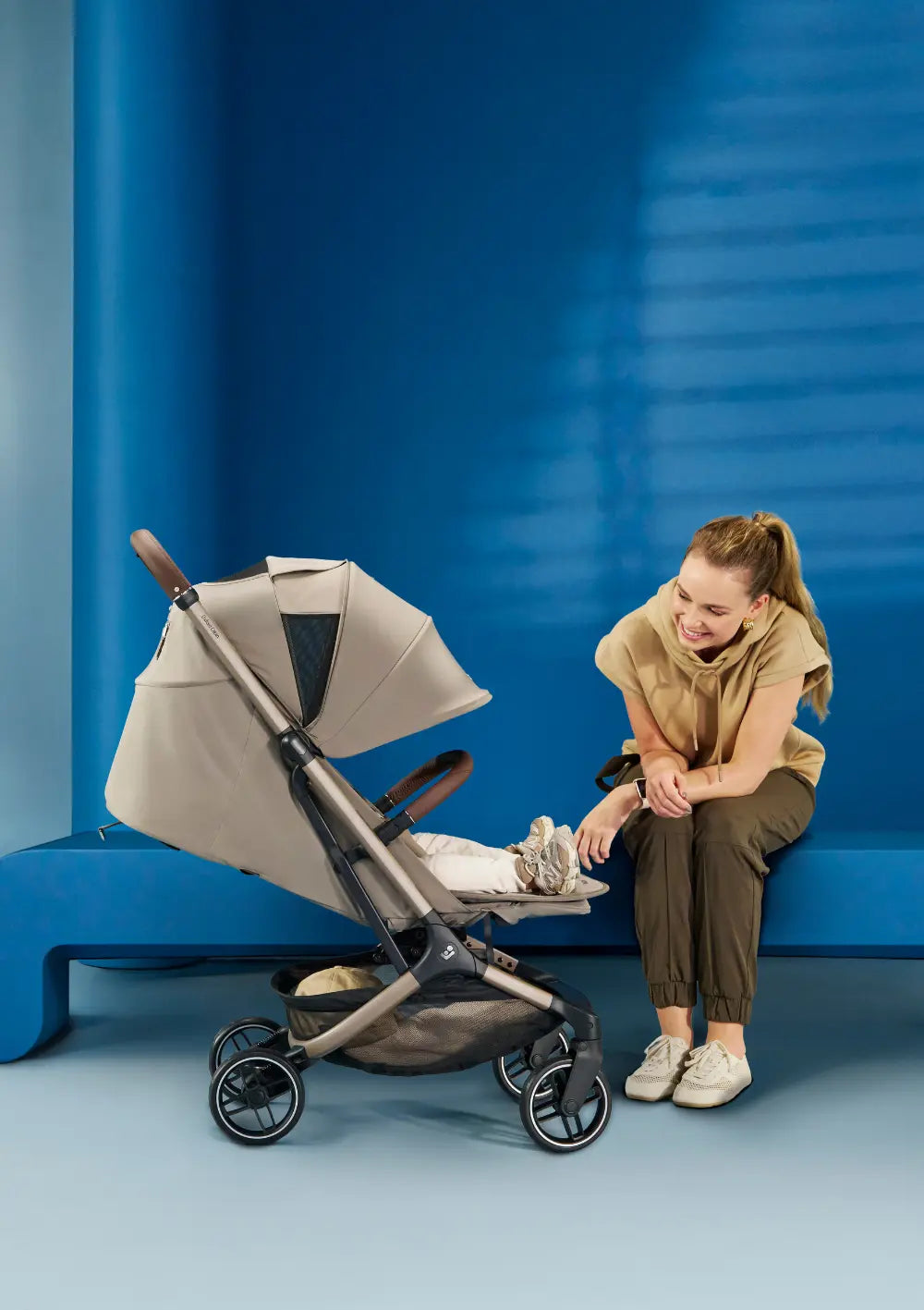 Frau sitzt auf Bank und schaut in den Maxi-Cosi Buggy 'Oxford Cabin' Oak Truffle zu ihrem Kind