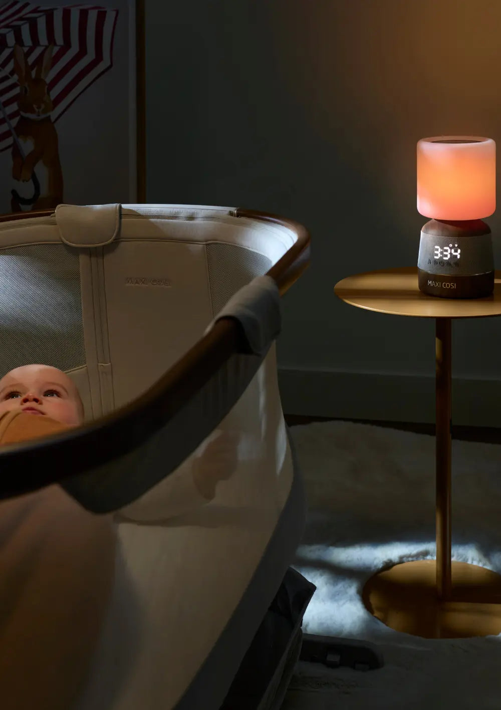 Sanfte Einschlafhilfe im Kinderzimmer: Das Maxi-Cosi Nachtlicht & Klang Connected Home Soothe Pro steht auf einem Tischchen neben einem Beistellbettchen mit Baby.