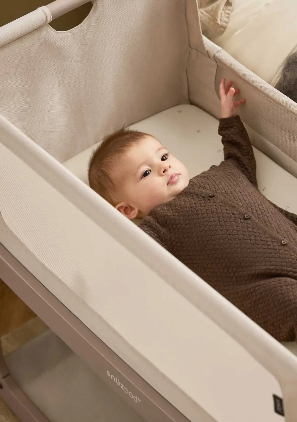 Ein Baby liegt in einem im SnüzPod 5 Beistellbett, das mit dem Spannbettlaken Cashmere mit Kreuzchen bezogen ist.