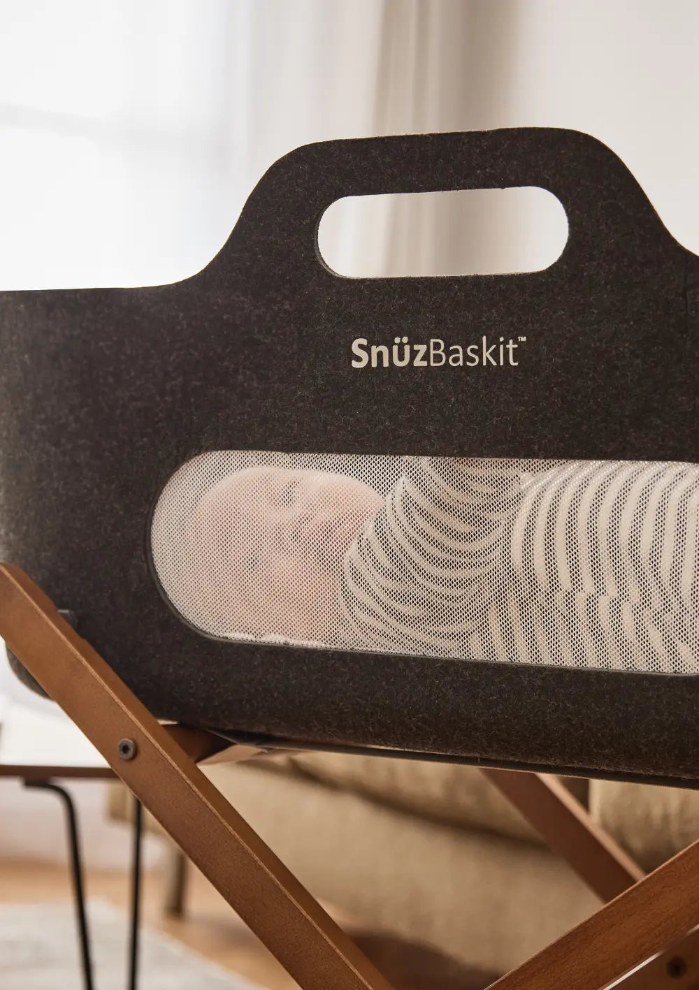 Ein schlafendes Baby im gestreiften Strampler ist durch das Mesh-Sichtfenster des Snüz Moseskorb inkl. Ständer SnüzBaskit Graphite-Walnuss zu sehen.