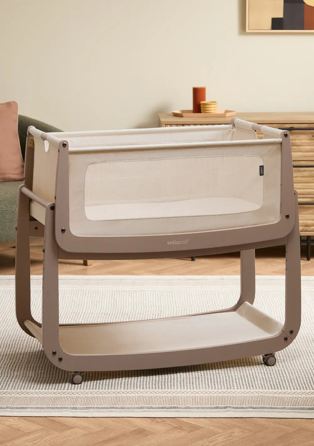 Das freistehende Snüz Beistellbett SnüzPod 5 Mocha aus dunkelbeigem Holz mit hellem Stoffbezug und praktischen Rollen am Gestell im Kinderzimmer.