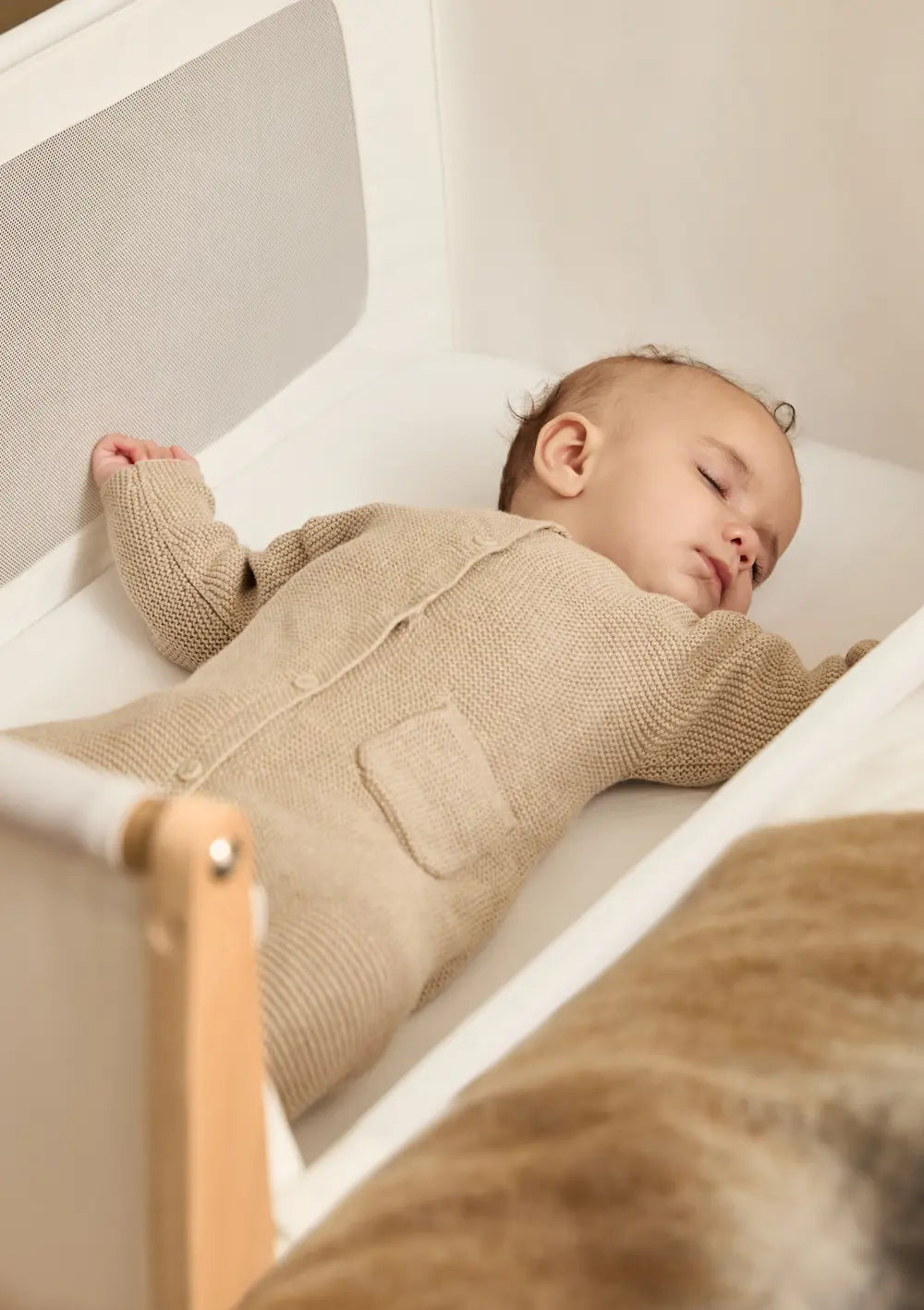 Ein Baby schläft friedlich im Snüz Beistellbett SnüzPod 5 Natur; die weich gepolsterte Umrandung sorgt für eine geschützte Schlafumgebung.