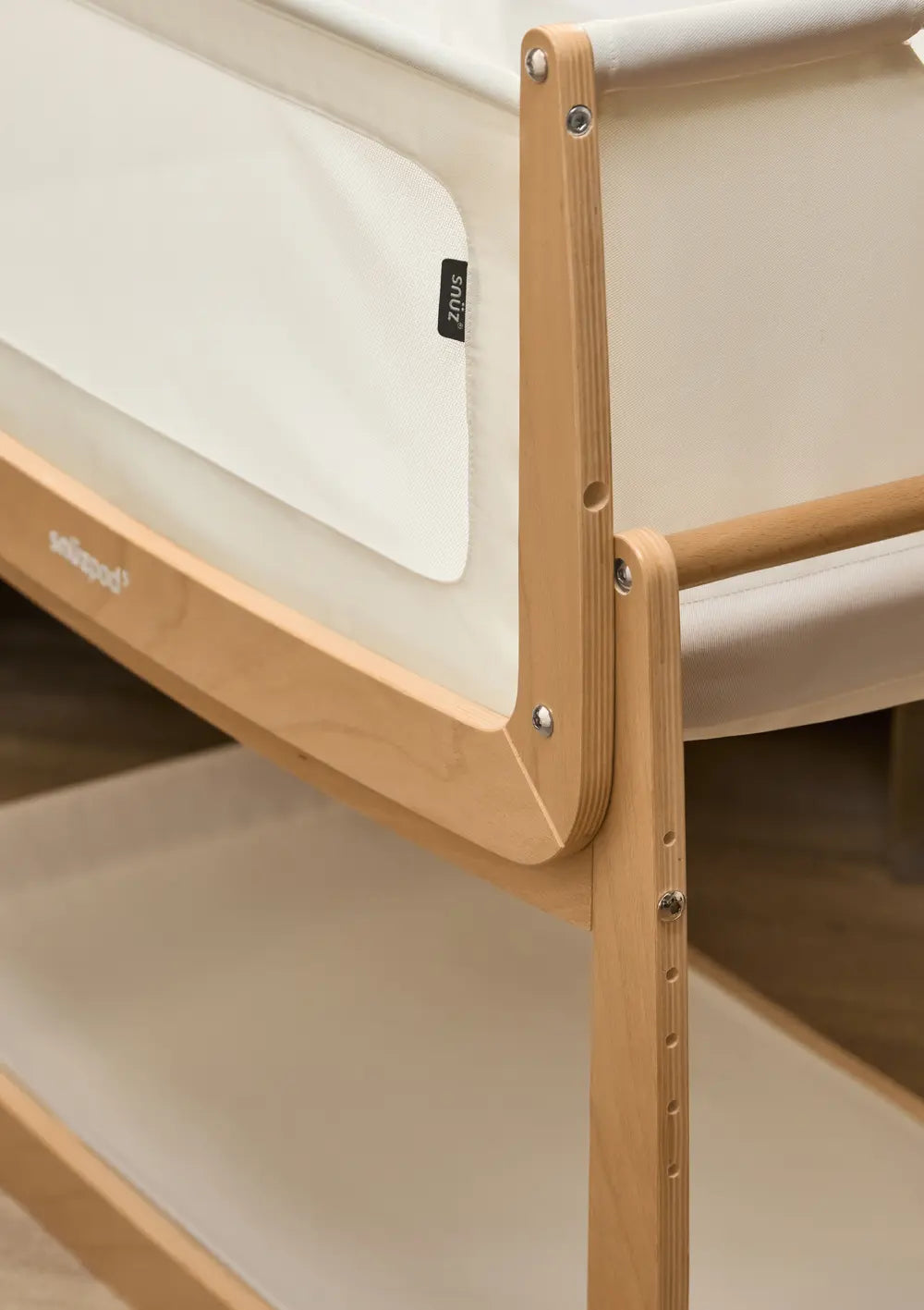 Detailansicht der stabilen Holzkonstruktion am Snüz Beistellbett SnüzPod 5 Natur mit atmungsaktivem Mesh-Gewebe und dem schwarzen Snüz-Markenlabel.