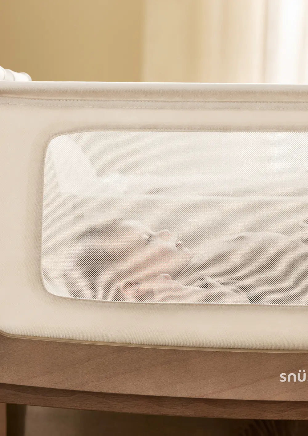 Ein schlafendes Baby ist in Nahaufnahme durch das transparente Mesh-Sichtfenster des Snüz Beistellbettes SnüzPod 5 Walnuss zu sehen; optimale Luftzirkulation im Fokus.