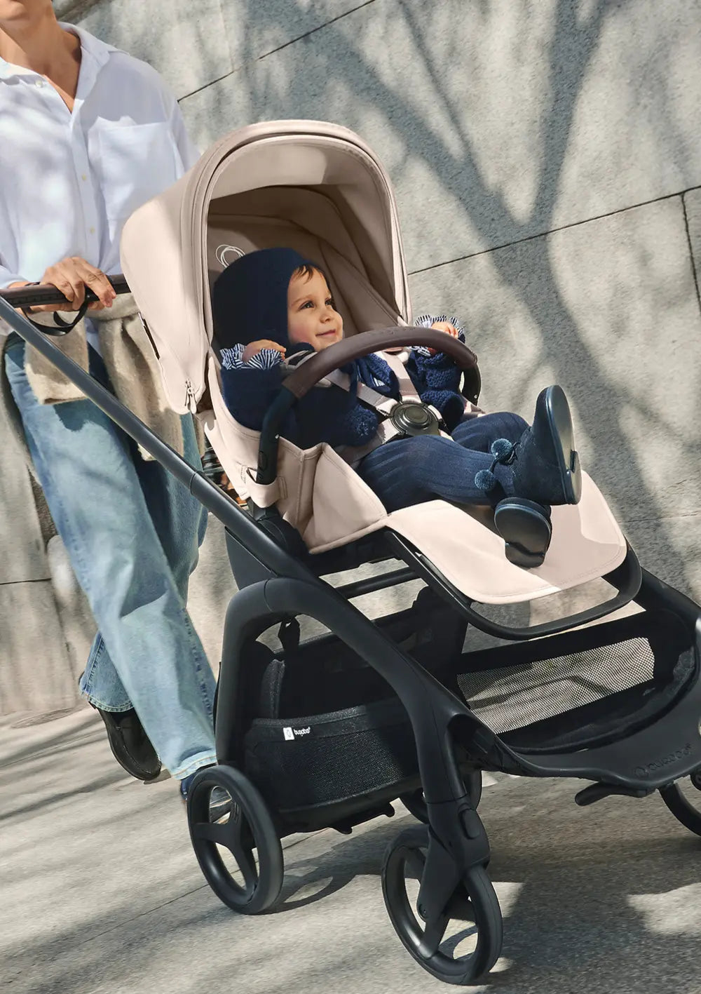 Der wendige Bugaboo Kinderwagen Dragonfly Plus im Einsatz beim Spaziergang; das lächelnde Kleinkind sitzt gut gesichert im beigefarbenen Sportsitz mit Sicherheitsbügel.