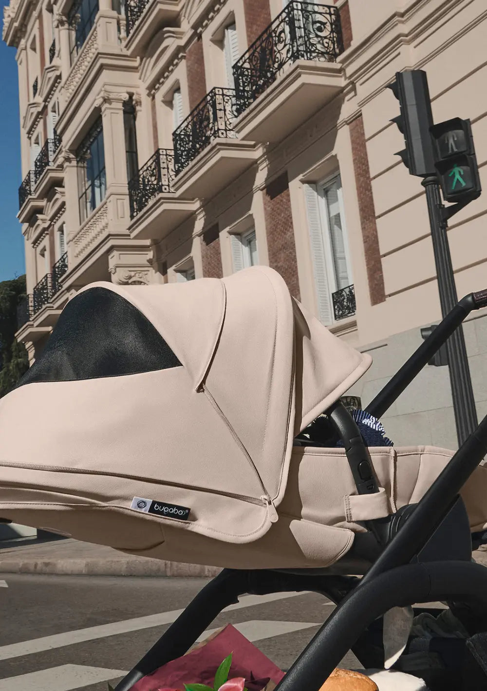 Nahaufnahme des Bugaboo Kinderwagens Dragonfly Plus an einer Ampel; das weit ausziehbare, beigefarbene Sonnenverdeck mit integriertem schwarzen Mesh-Lüftungsfenster schützt das Kind vor der Sonne.