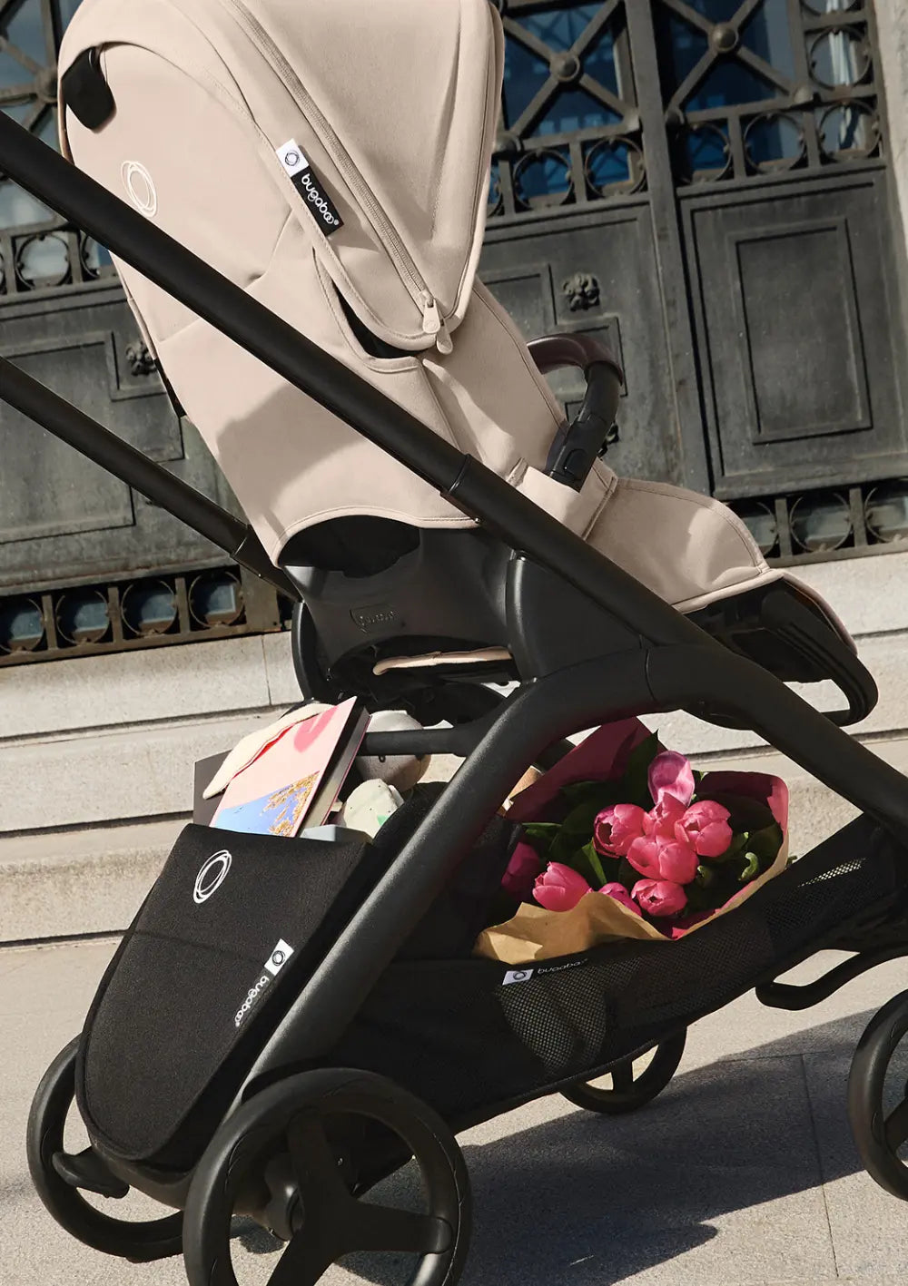 Nahaufnahme des Bugaboo Kinderwagens Dragonfly Plus; großzügig gestaltete Untergestellablage mit integrierter Tasche ist mit Blumen und weiteren Sachen befüllt.