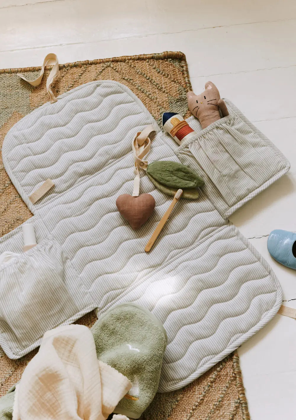 Die geöffnete, wattierte Dear April Wickelunterlage River Dew Stripe mit feinen Streifen und integrierten Taschen für Windeln und Pflegezubehör liegt ausgebreitet auf dem Boden.