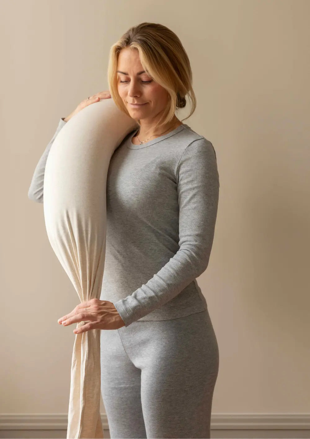 Eine Frau in grauer Kleidung trägt das flexible bbhugme Stillkissen Soft White zusammengefaltet über ihrer Schulter, um die kompakte Transportierbarkeit des Kissens zu demonstrieren.