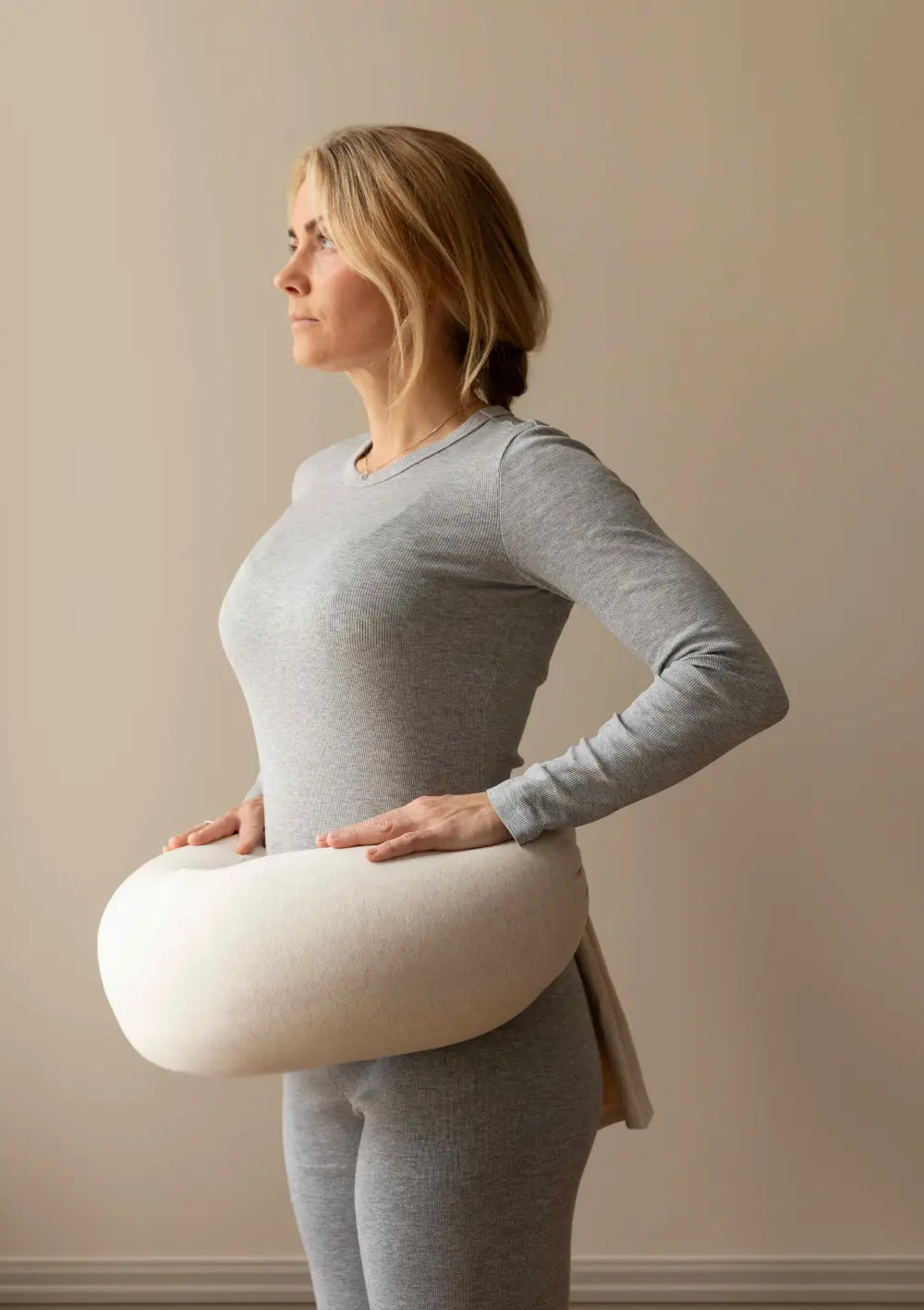 Seitenansicht einer Frau, die das cremefarbene bbhugme Stillkissen Soft White um ihre Taille gelegt hat, um die Passform als stützende Bauch- und Stillhilfe zu zeigen.