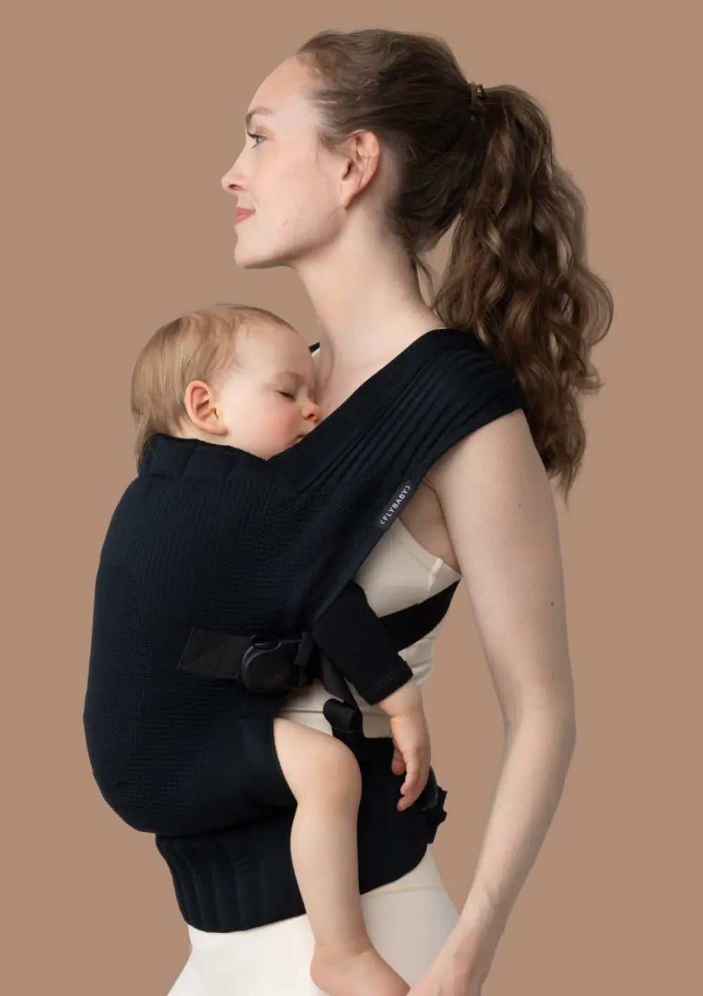 Frau trägt ihr Kleinkind in der Flybaby Kleinkindtrage Black vor dem Bauch.