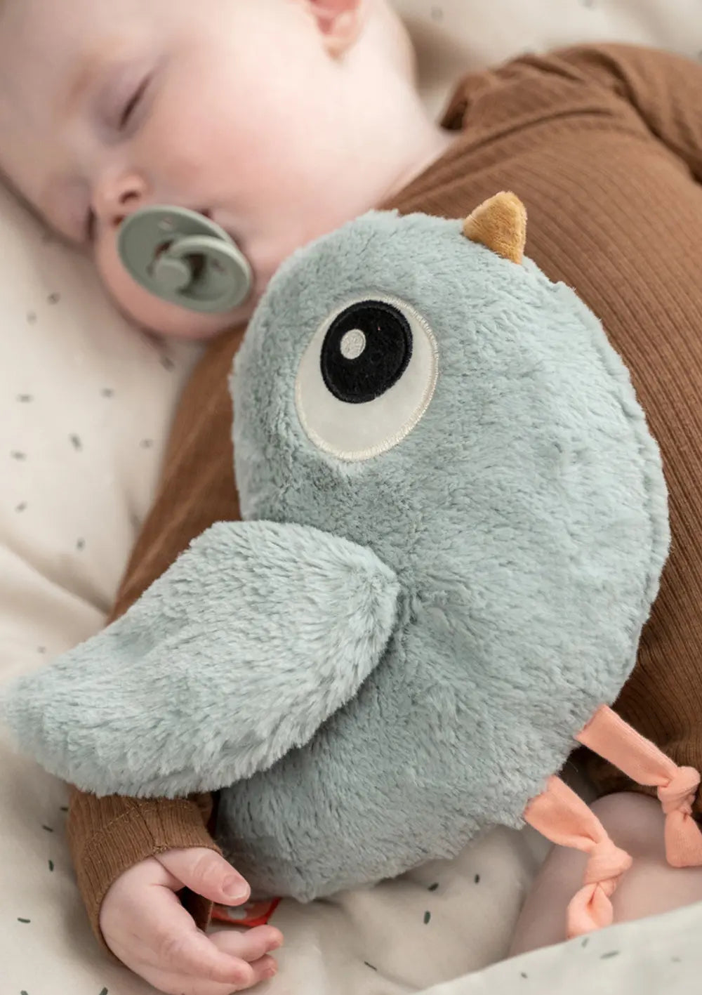 Ein schlafendes Baby mit Schnuller im Mund und Done by Deer Kuscheltier 'Birdee'klein blau im Arm.
