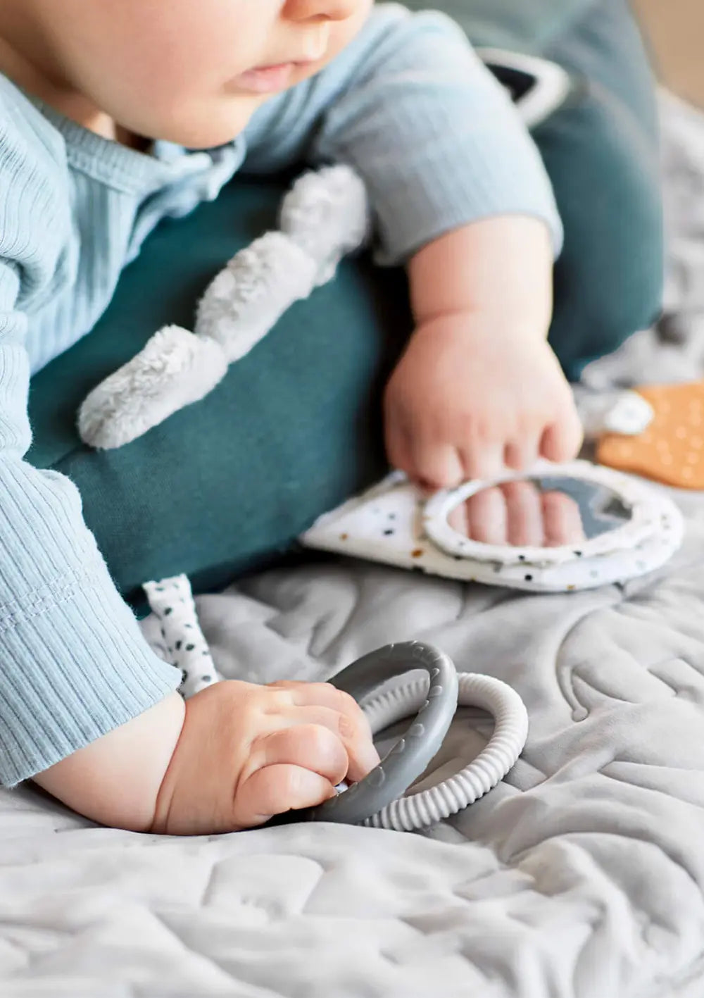 Nahaufnahme eines Babys, das über dem dunkelgrünen Done by Deer Spielkissen Croco Grün liegt und mit den Händen nach den befestigten Greifringen und dem kleinen Entdeckerspiegel tastet.