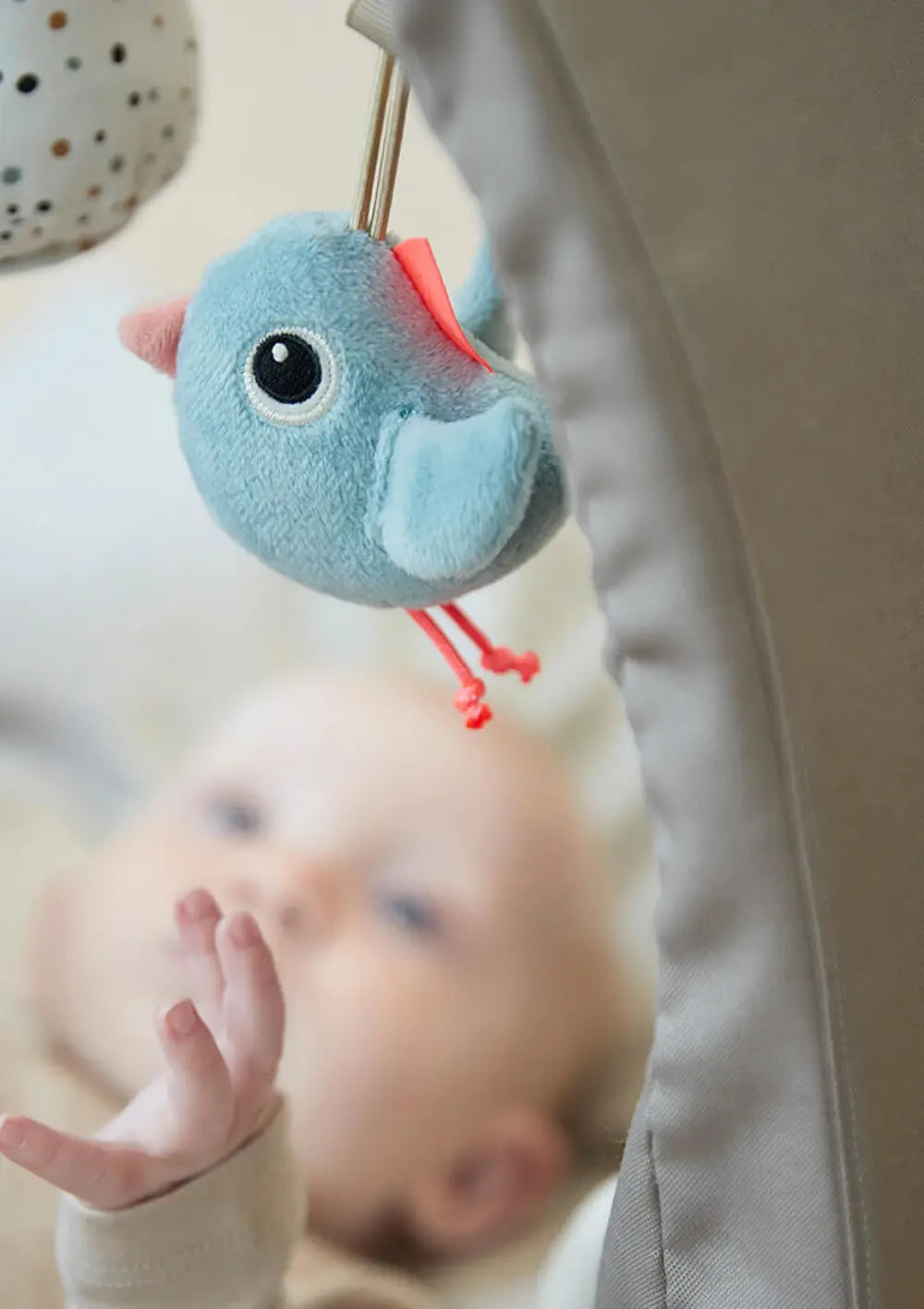 Ein Baby liegt unter dem Done by Deer Spielbogen Activity Gym Lalee Sand und streckt die Hand nach dem hellblauen Plüschvogel Birdee aus, der direkt über ihm am Bogen hängt.