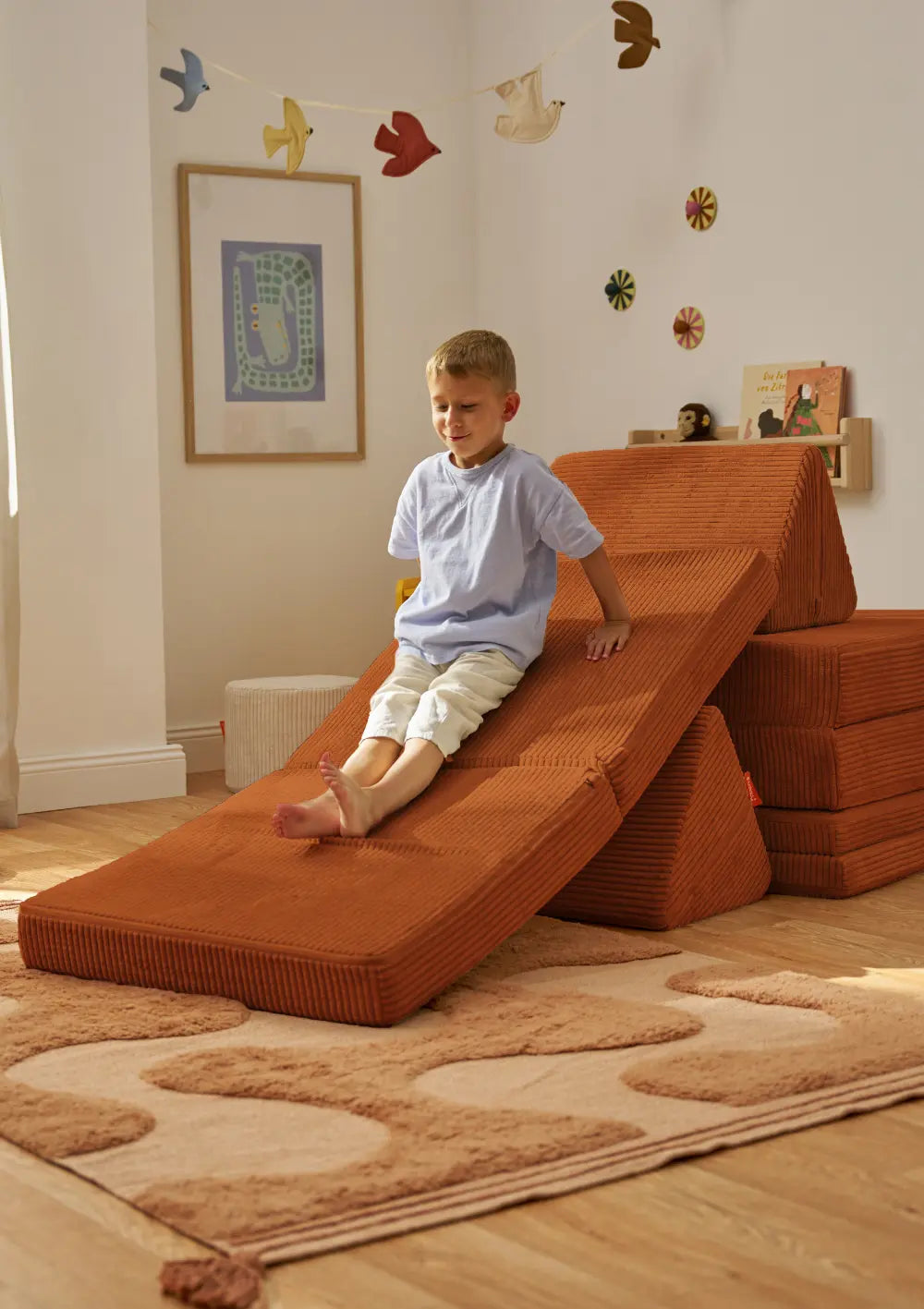 Kind nutzt das Funzy Spielsofa Cord Rost Orange als Spielrutsche im Kinderzimmer