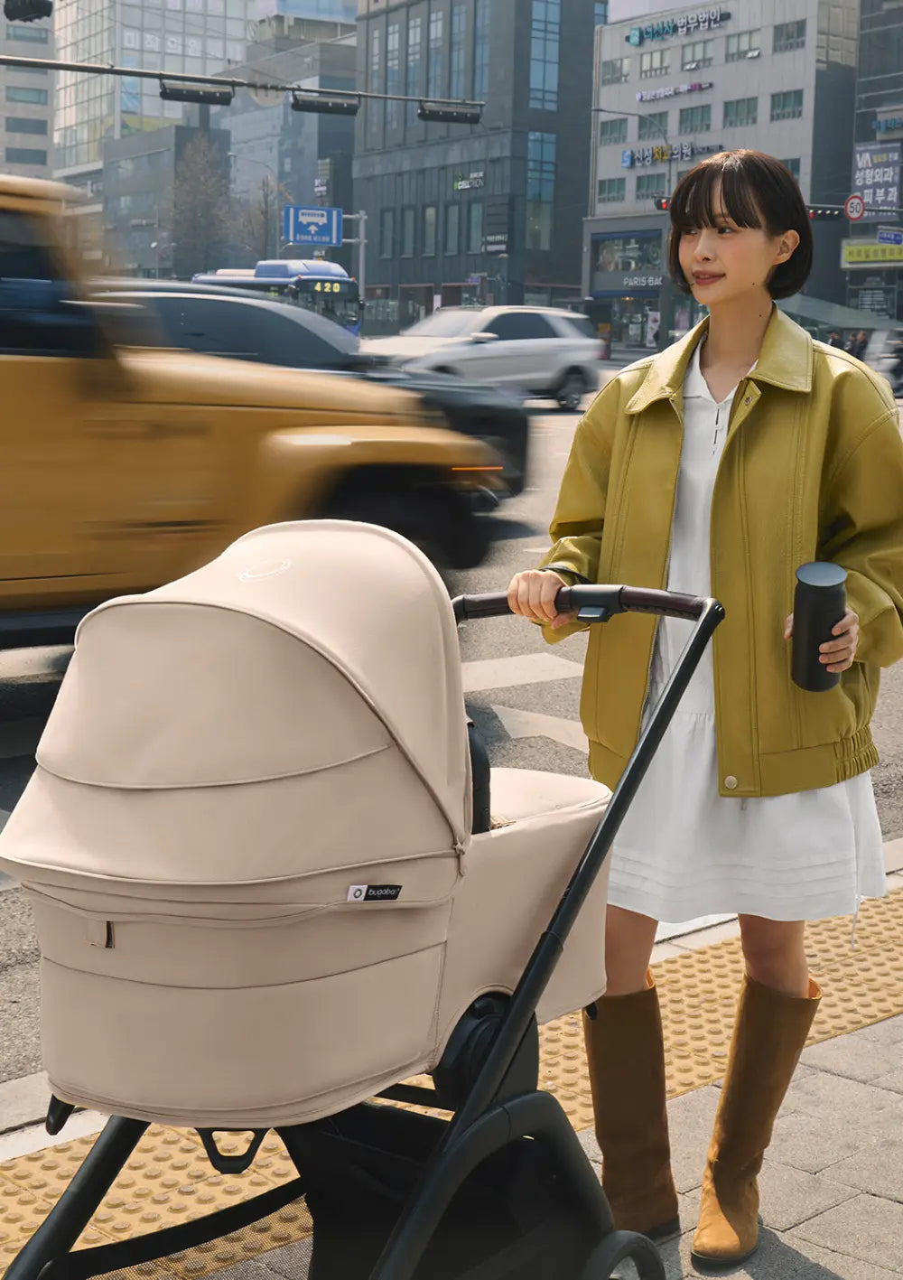 Eine Frau steht mit dem Kinderwagen und der aufgebauten Bugaboo Liegewanne für den Kinderwagen Dragonfly Plus an einer städtischen Straßenkreuzung.