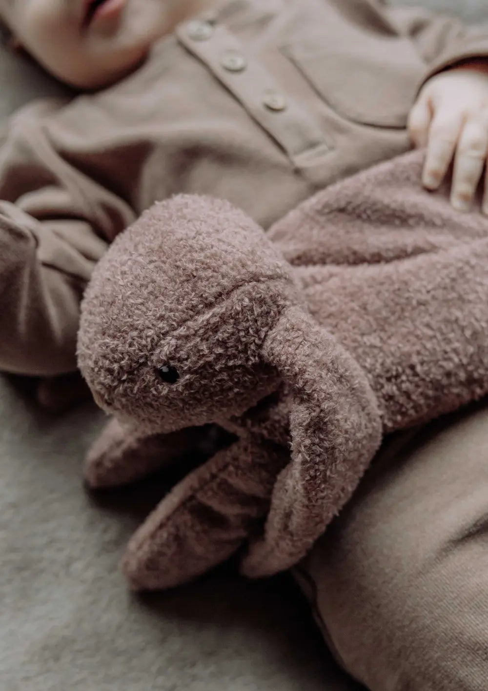 Baby liegt mit dem flow AMSTERDAM Wärmekissen Hase 'Milo' chocolate auf dem Bauch im Bett