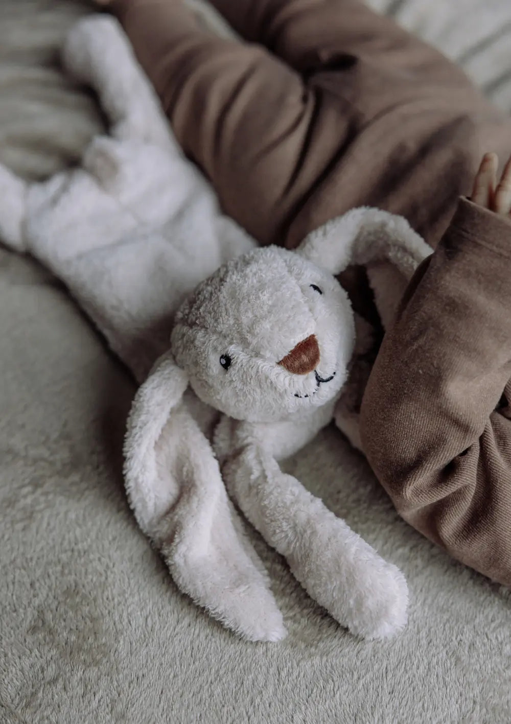 Kind liegt im Bett, mit dabei: flow AMSTERDAM Wärmekissen Hase 'Milo' blush