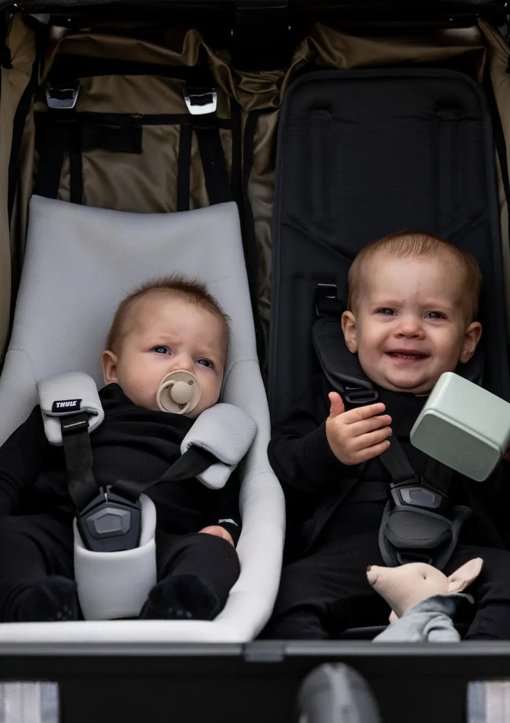 Komfort für die Kleinsten: Detailansicht von zwei Babys im Thule Multisport-Fahrradanhänger Chariot Cross 2 Double Faded Khaki, eines davon im Thule Infant Sling Sitzverkleinerer.