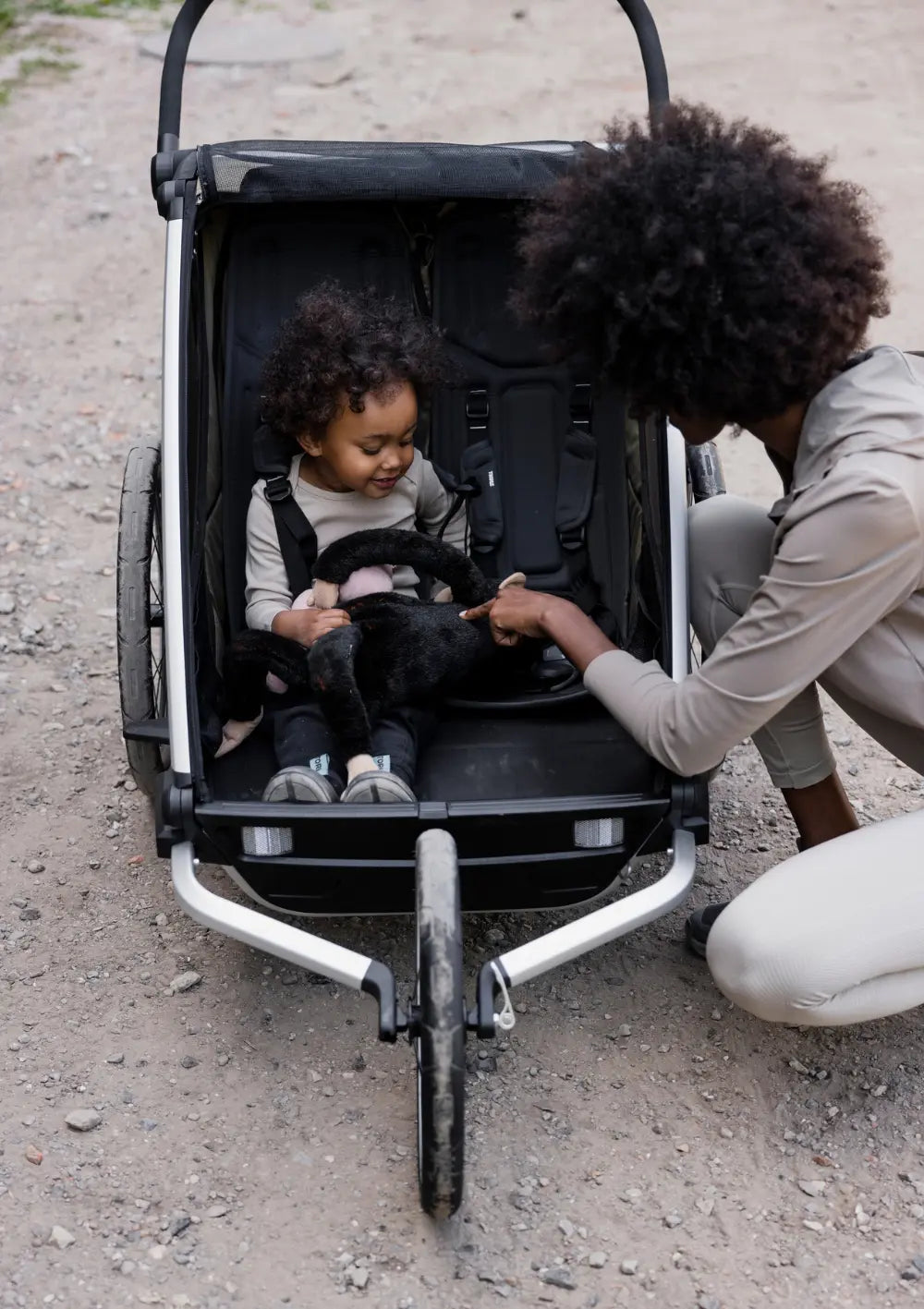 Frontalansicht des Zweisitzers mit dem installierten Thule All-Terrain Kit für Fahrradanhänger Chariot 2 Double; eine Mutter kümmert sich um ihr angeschnalltes Kleinkind im Wagen.