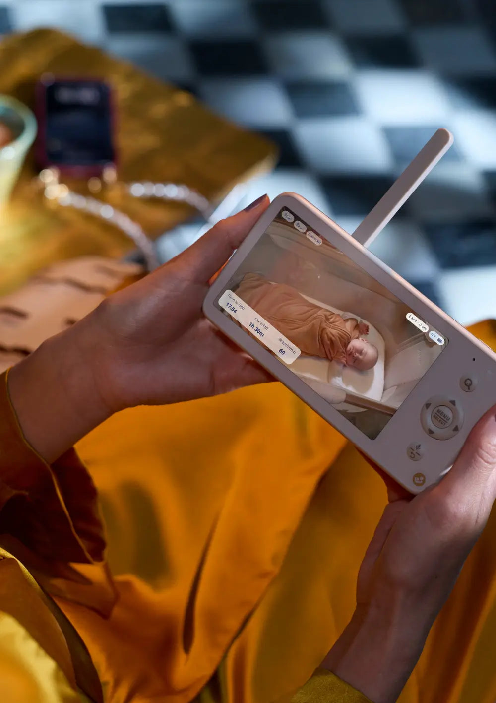 Eine Person hält das Display der Elternstation des Maxi-Cosi Babyphone Connected Home See 2 Plus in den Händen und überwacht das schlafende Kind per Live-Video.