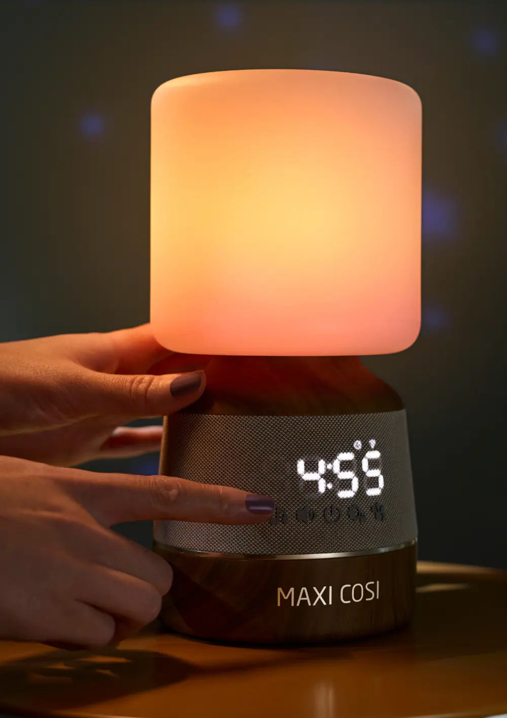 Nahaufnahme der manuellen Bedienung: Eine Hand berührt die Touch-Tasten an der Unterseite des Maxi-Cosi Nachtlicht & Klang Connected Home Soothe Pro, das eine digitale Uhrzeit anzeigt.