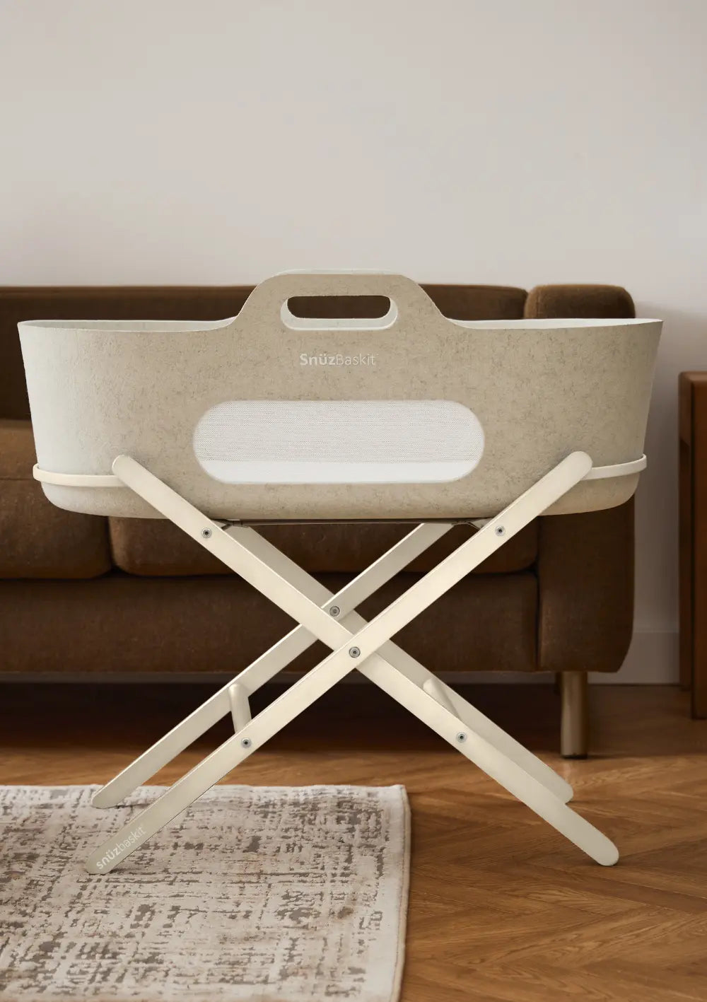 Der stilvolle Snüz Moseskorb inkl. Ständer SnüzBaskit Barley-Cashmere komplett aufgebaut auf seinem klappbaren, cremefarbenen Holz-X-Gestell auf Parkettboden im Wohnzimmer.