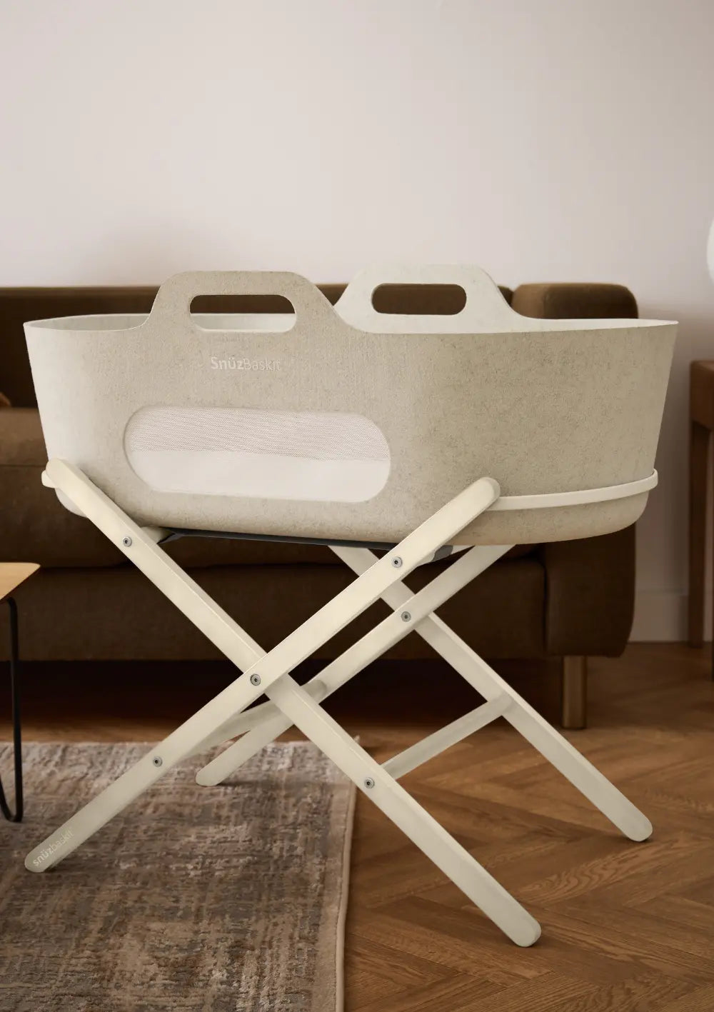 Der stilvolle Snüz Moseskorb inkl. Ständer SnüzBaskit Barley-Cashmere komplett aufgebaut auf seinem klappbaren, cremefarbenen Holz-X-Gestell auf Parkettboden im Wohnzimmer.