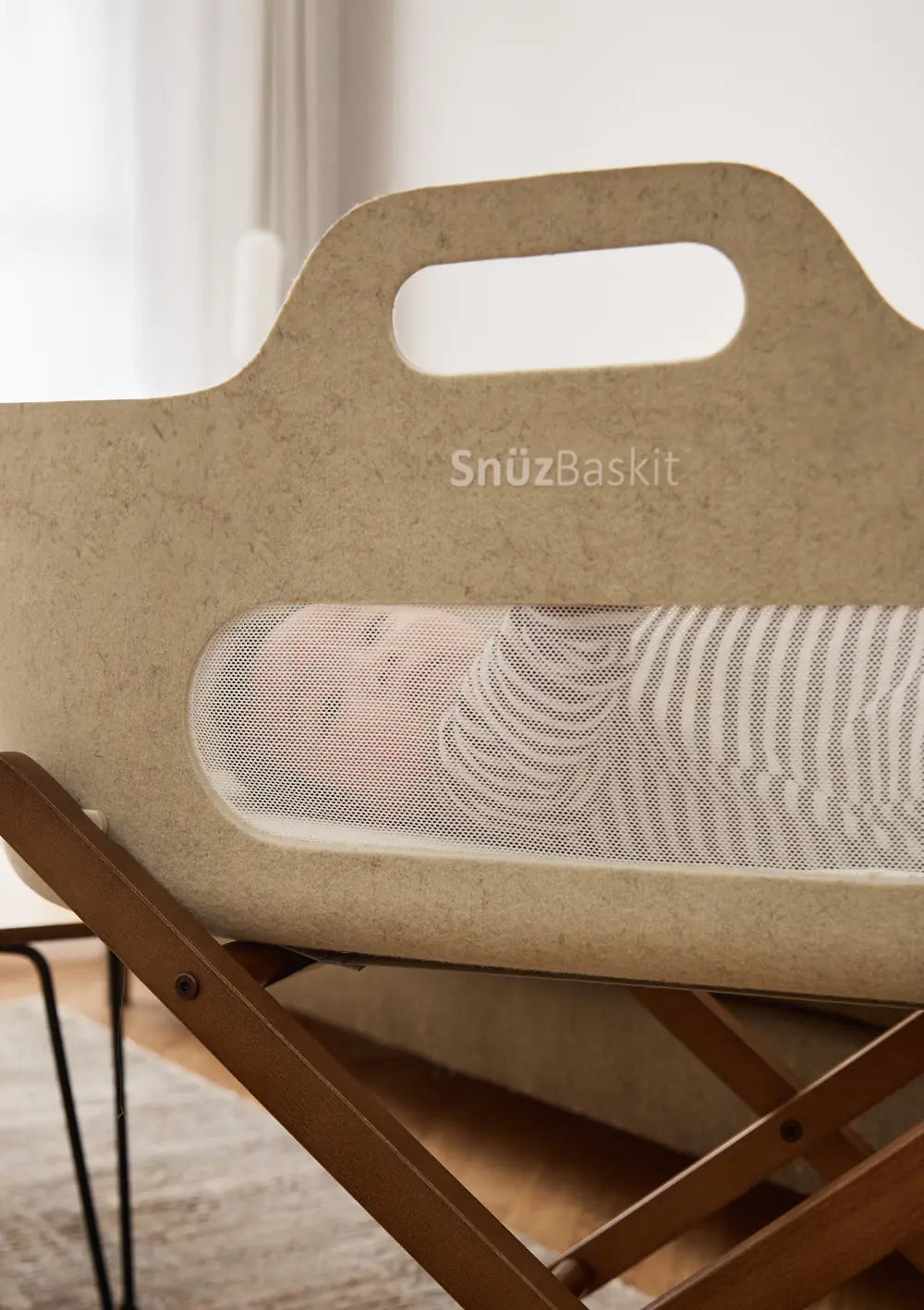 Ein Baby ist in Nahaufnahme durch das transparente Mesh-Sichtfenster des hellbeigen Snüz Moseskorb inkl. Ständer SnüzBaskit Barley-Walnuss zu sehen.