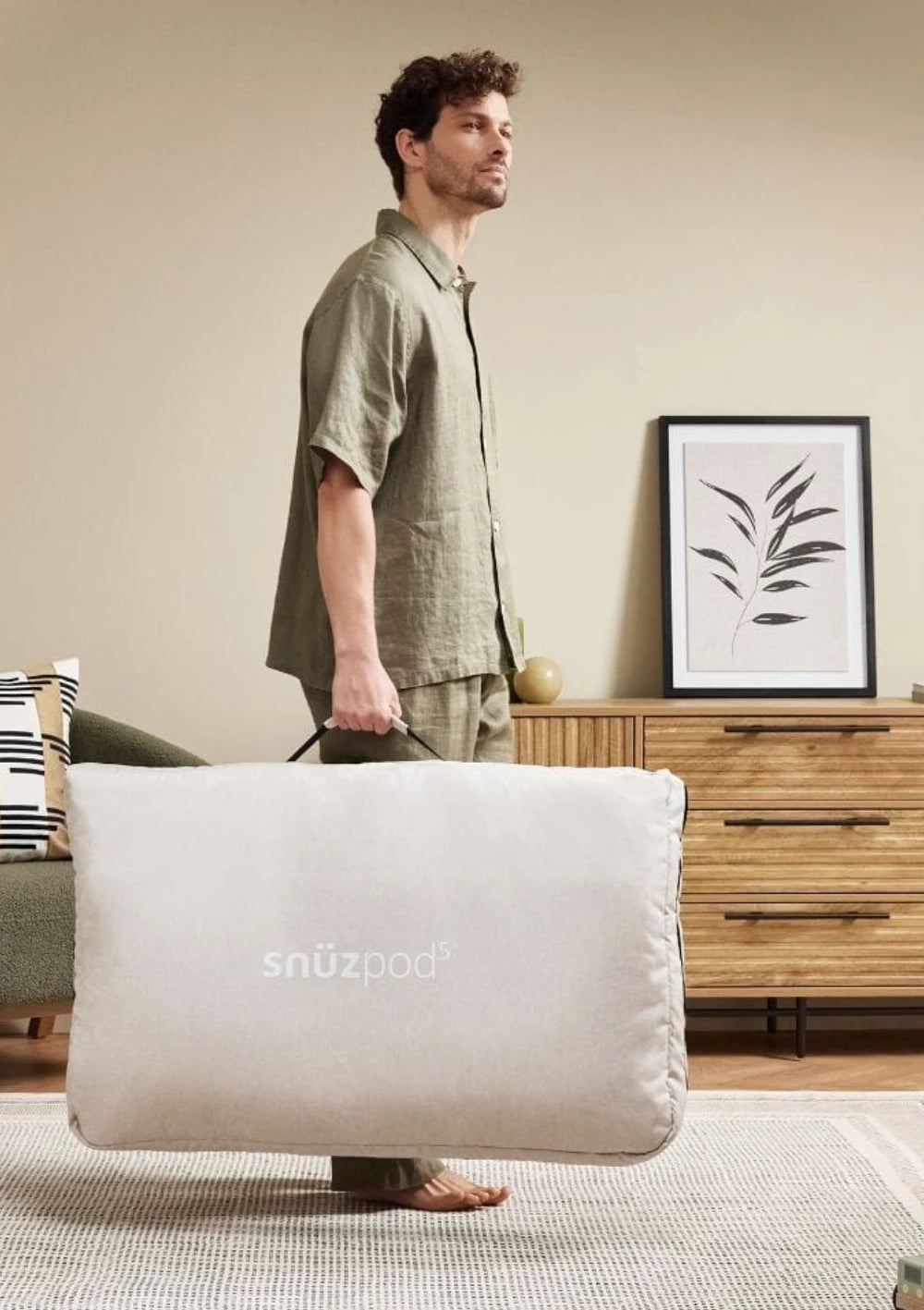Ein Mann trägt das Beistellbett SnüzPod 5 in der Aufbewahrungstasche mit praktischen Tragegriff