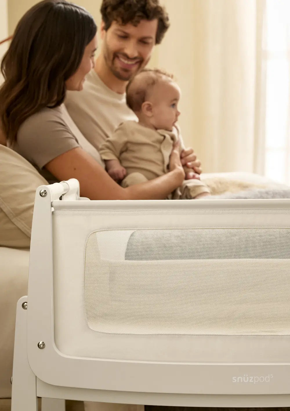 Ein Elternpaar mit Baby neben dem Snüz Beistellbett SnüzPod 5 Cashmere.