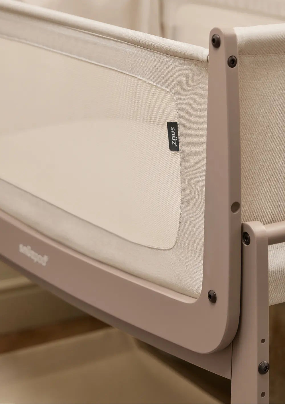 Detailansicht des moccafarbenen Holzrahmens am Snüz Beistellbett SnüzPod 5 Mocha mit atmungsaktivem Mesh-Gewebe und dem schwarzen Snüz-Markenlabel.