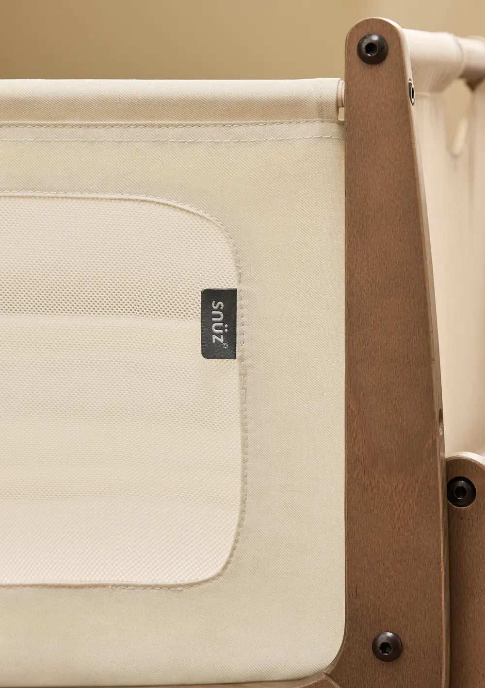 Detailansicht des dunkelbraunen Walnussholz-Rahmens am Snüz Beistellbett SnüzPod 5 Walnuss mit dem kleinen, schwarzen Snüz-Markenlabel.