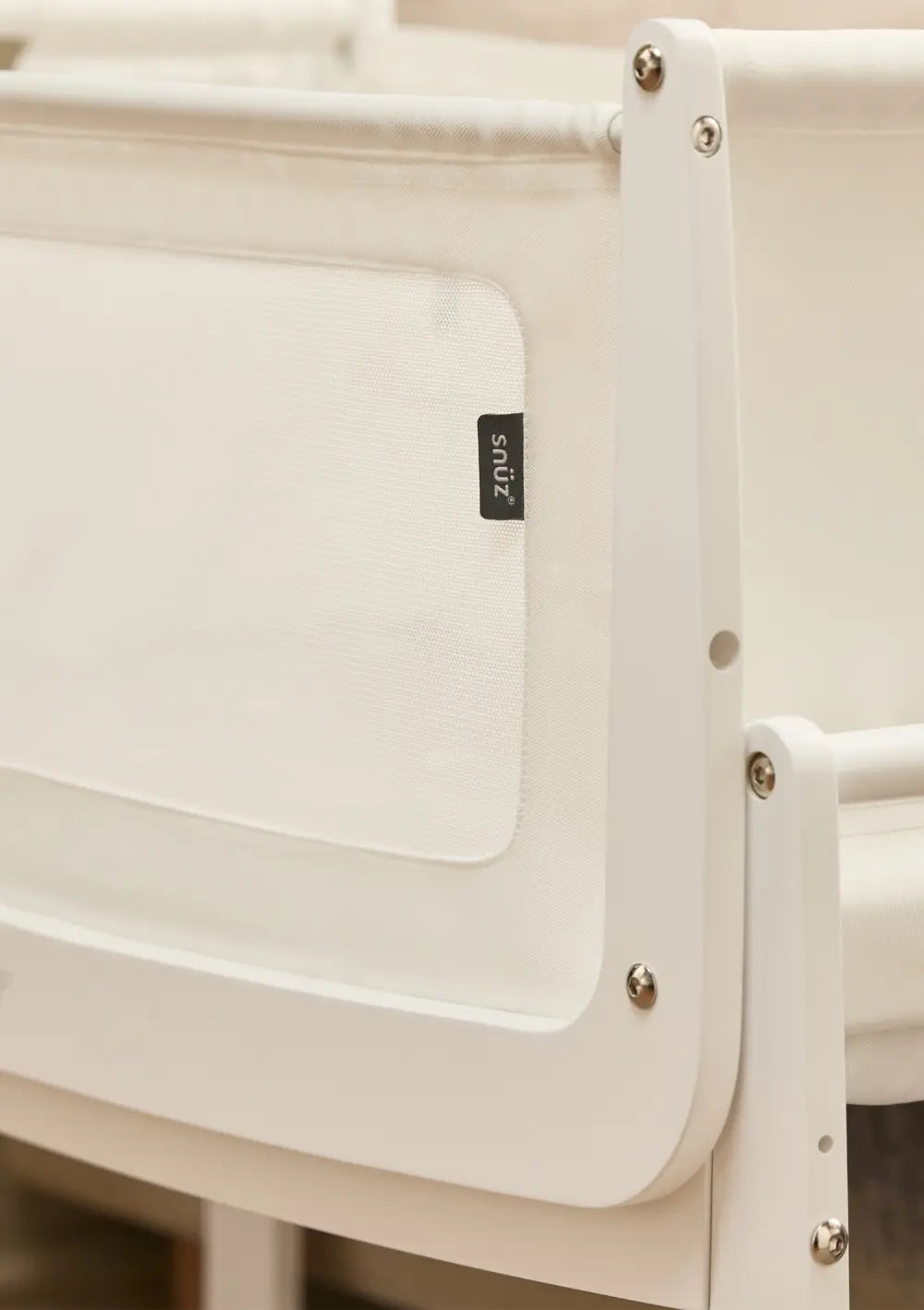 Detailansicht des weißen Holzrahmens und der hochwertigen Textilverarbeitung am Snüz Beistellbett SnüzPod 5 mit dem kleinen, schwarzen Snüz-Markenlabel.