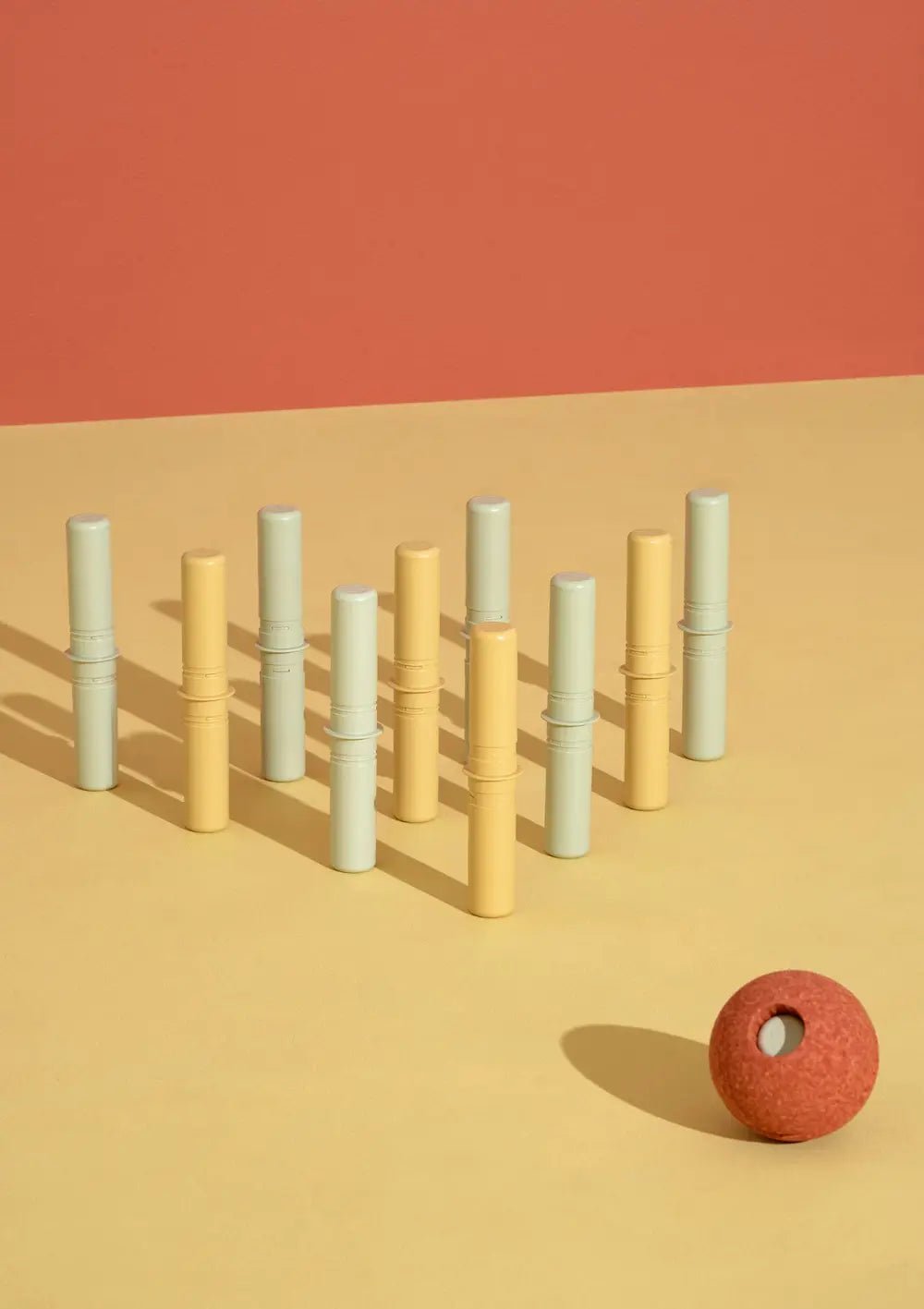 Ein aufgebautes Kegelspiel aus hellgelben und mintgrünen Verbindungsstiften, auf das ein orangefarbener Ball aus dem MODU 3er-Set Schaumstoffbälle Orange auf einer gelben Fläche ausgerichtet ist.
