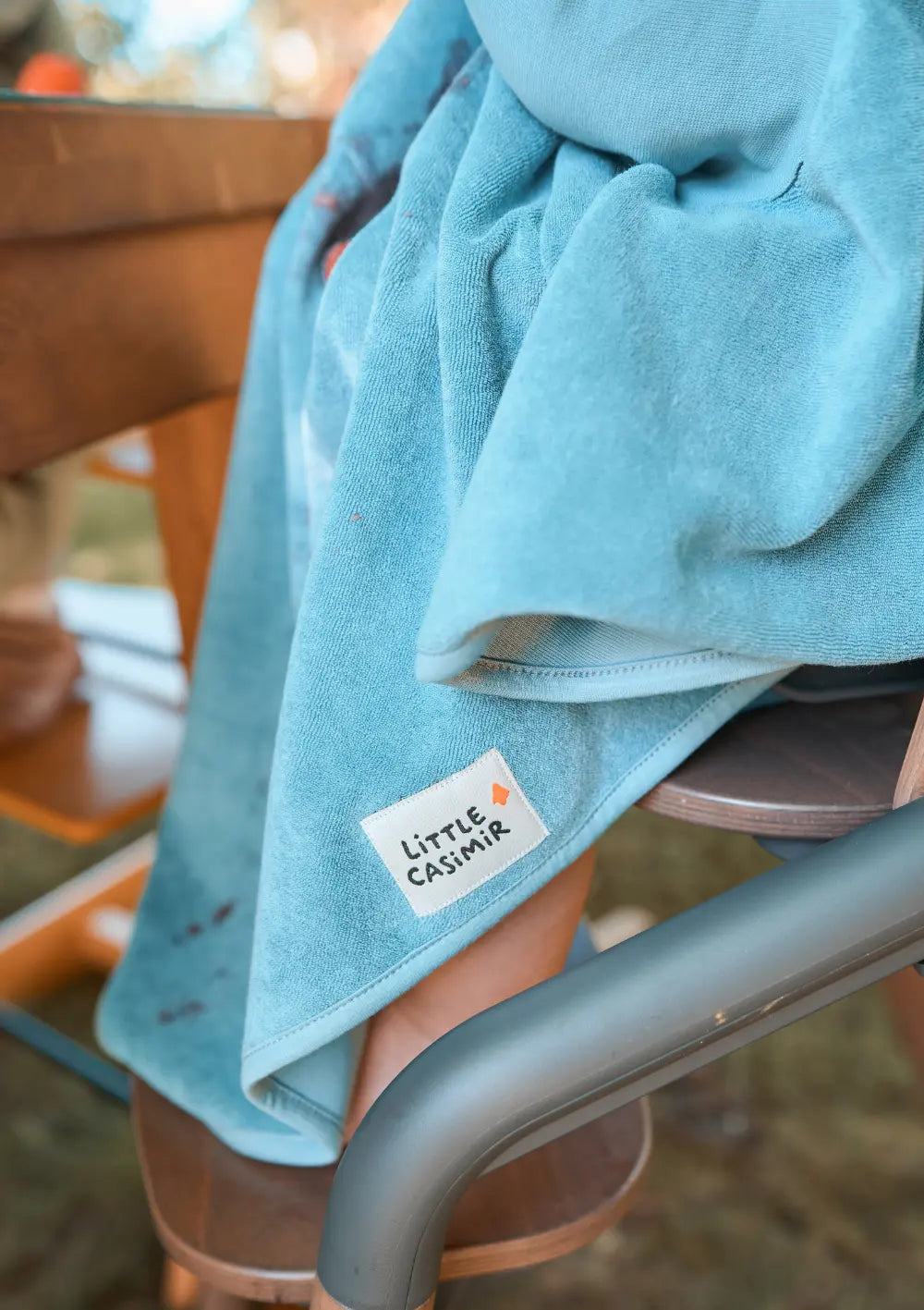 Der weiche, blaugrüne Frottee-Stoff des Little Casimir Langarm-Lätzchens Boo Dusty Ocean mit dem weiß aufgenähten Marken-Label.