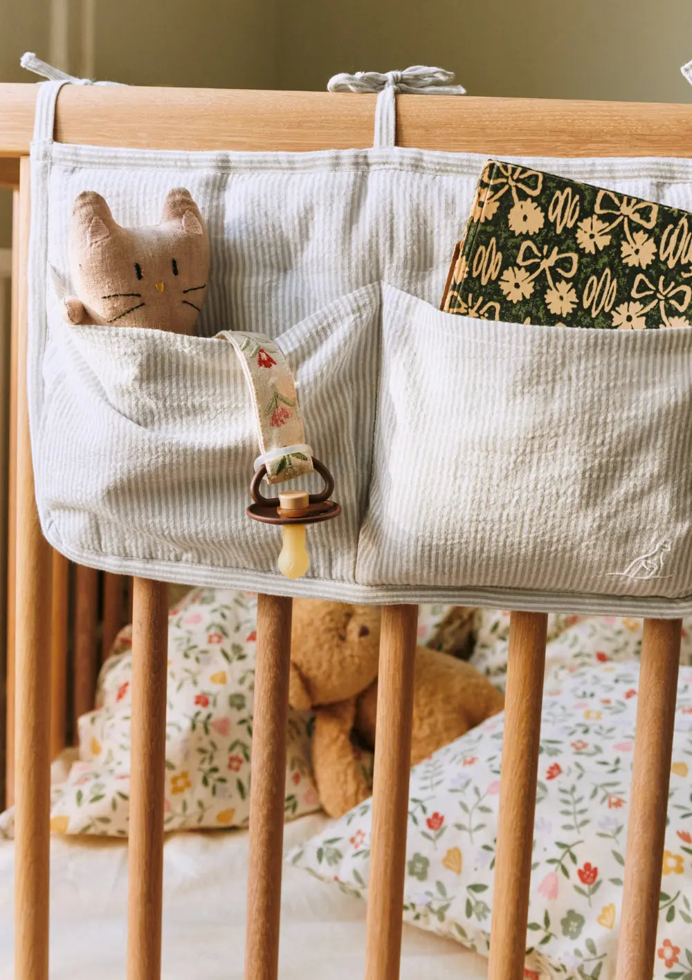 Die am Gitterbett befestigte Dear April Betttasche Polly Dew Stripe im dezenten Streifen-Look hält wichtige Utensilien wie ein kleines Kuscheltier und ein Buch griffbereit geordnet.