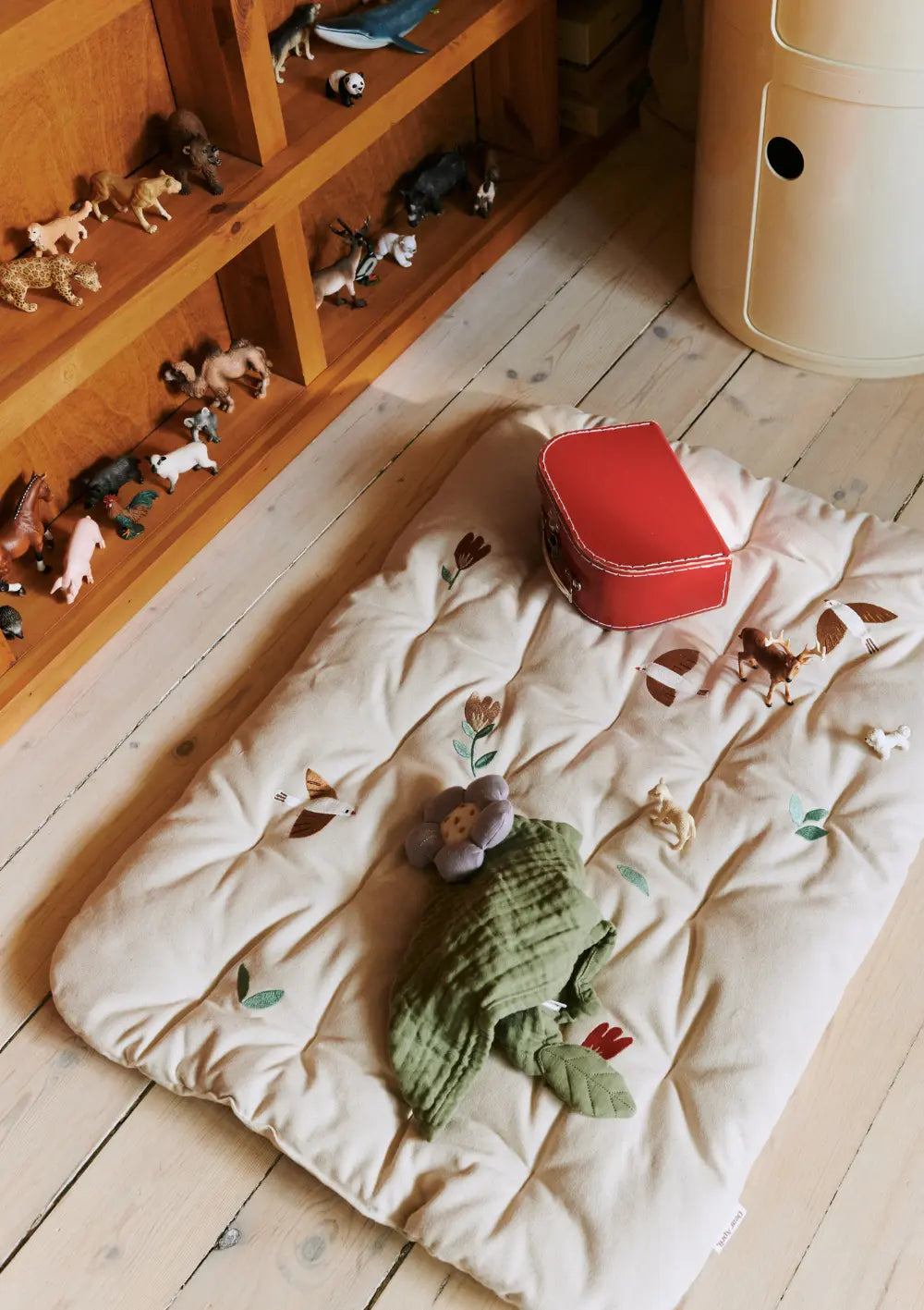 Die gepolsterte Dear April Spieldecke Morris Songbirds liegt auf hellem Holzboden; auf der Decke mit zarten Vogel- und Pflanzenstickereien befinden sich ein kleiner roter Spielzeugkoffer, ein grünes Mulltuch und Spielfiguren.