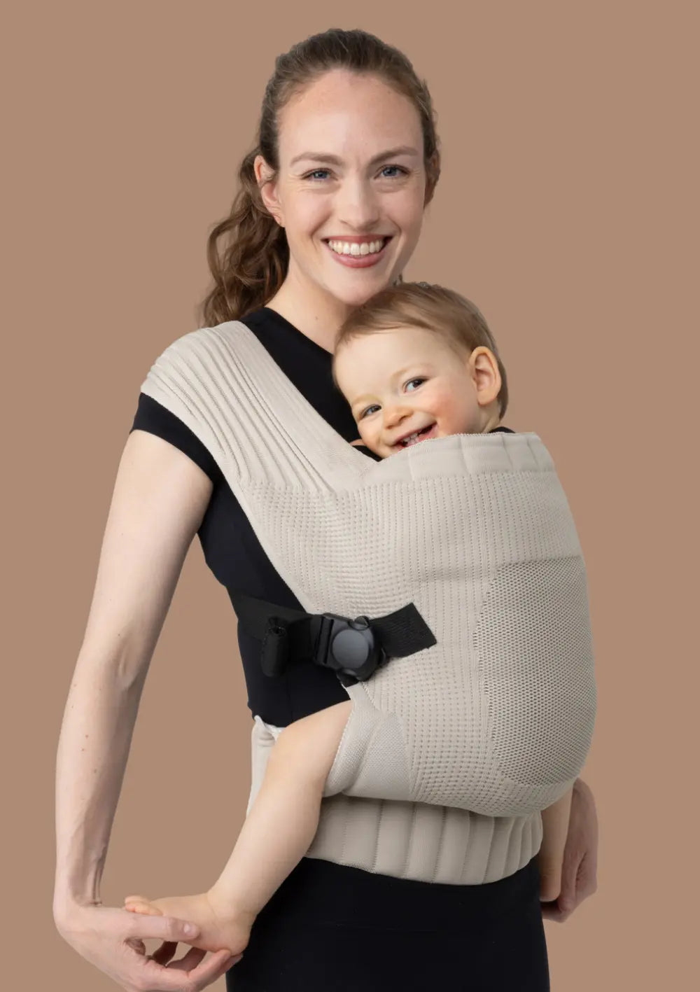 Frau trägt ihr Kleinkind in der Flybaby Kleinkindtrage Creme vor dem Bauch.