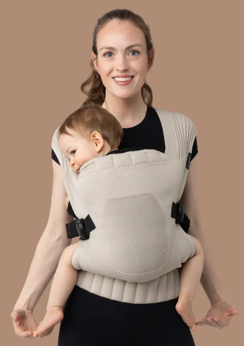 Frau trägt ihr Kleinkind in der Flybaby Kleinkindtrage Creme vor dem Bauch.