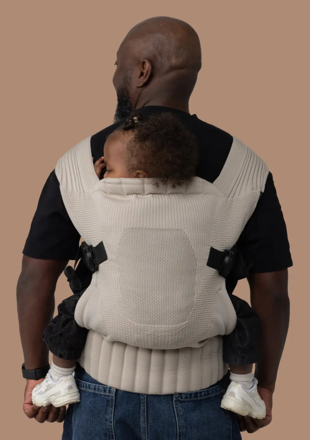 Mann trägt sein Kleinkind in der Flybaby Kleinkindtrage Creme sicher auf dem Rücken.