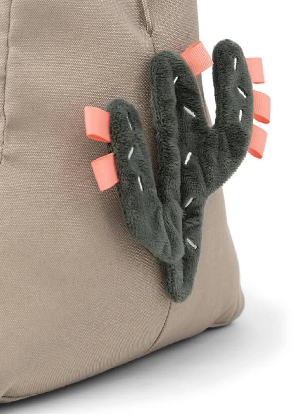 Detailaufnahme der sandfarbenen Standfläche des Done by Deer Spielbogens Activity Gym Lalee Sand, an der ein weicher, dunkelgrüner Plüsch-Kaktus mit korallenfarbenen Entdecker-Schlaufen angebracht ist.