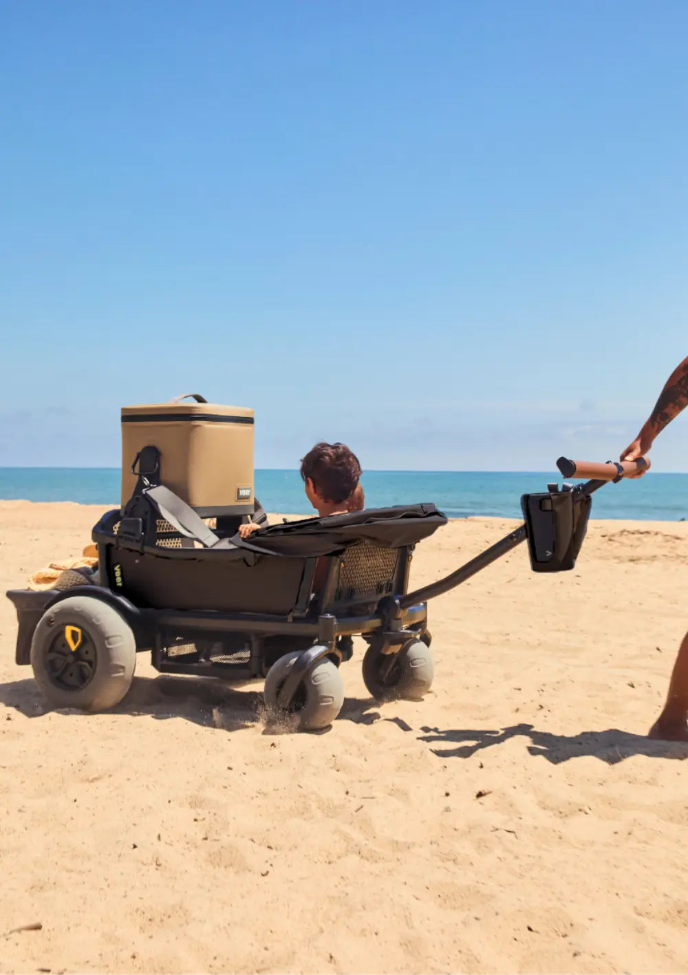 Ein Veer Cruiser wird an einem sonnigen Tag über feinen Sandstrand gezogen; ausgestattet ist er mit den breiten, grauen Veer Strandräder Beach Wheels für Cruiser und Cruiser XL für müheloses Vorankommen im Sand.