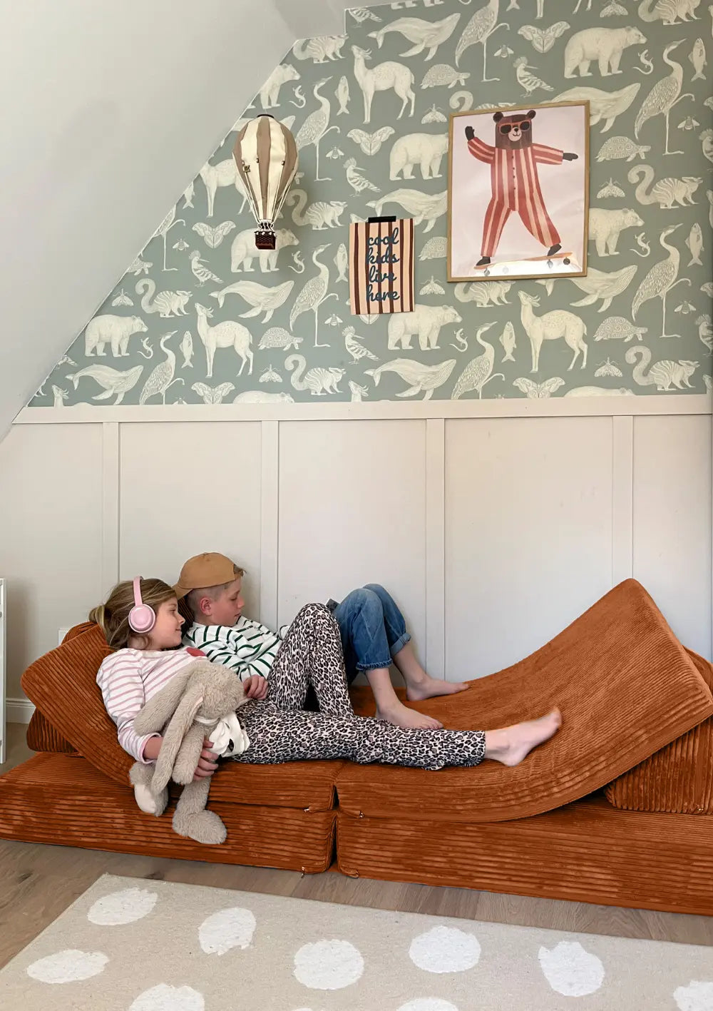 Zwei Kinder liegen gemütlich auf dem Funzy Spielsofa Cord Rost Orange im Kinderzimmer